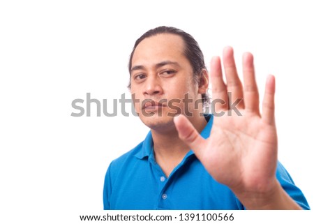 Portrait of a cute handsome young Asian man with long hair showing stop gesture with angry face, image with selective focus
