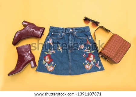floral embroidered ,bird pattern skirt jeans with boots shoes and handbag ,sunglasses on yellow background 
