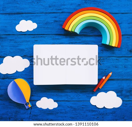 Creative children's waldorf montessori school or travel concept. Paper crafts, colored pencils, wood rainbow and blank book for text on blue table. Kids art class, kindergarten, preschool background