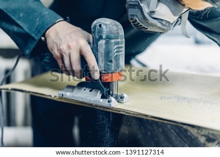  A carpenter cuts a board with an electric jigsaw. manufacture of skateboards. he has protective clothing and mask. 4k