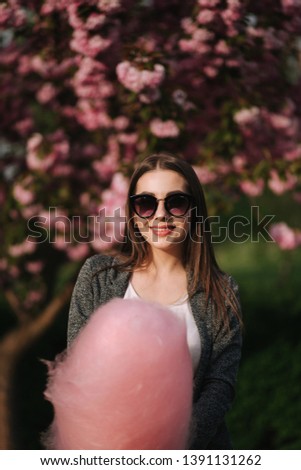 Close up portrait of smiling girl holding cotton candy in hands. Girl dressed in grrey blazer and sunglasses