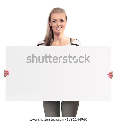 YOUNG PRETTY WOMAN HOLDING WHITE BLANK BANNER AND SMILING HAPPY WHILE STANDING AND LOOKING AHEAD ISOLATED ON WHITE BACKGROUND