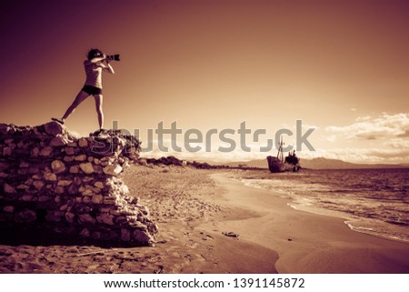 Tourism vacation and travel. Woman tourist on beach taking photo with camera, shipwreck in the background