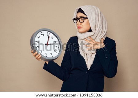 hijab woman in burqa glasses looks at a wall clock on a beige background time                              