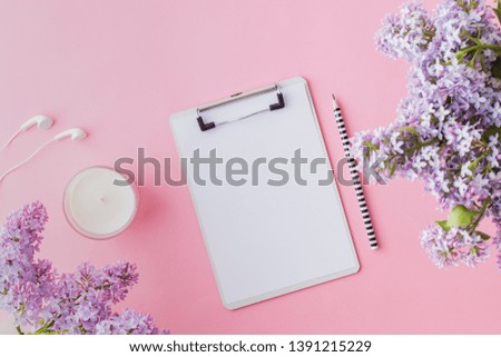 Flat lay blogger or freelancer workspace with a mockup clipboard and branches of lilac on a pink background
