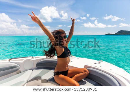Luxury yacht party woman enjoying freedom having fun with arms up in the wind on high end boat summer vacation trip. Laughing young Asian woman in elegant black bikini, long hair and sun tanned body.