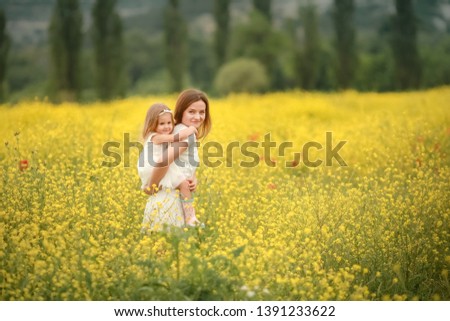 A Happy family: mother with young girl stand hand in hand on a green field against the background of coniferous forest and mountains