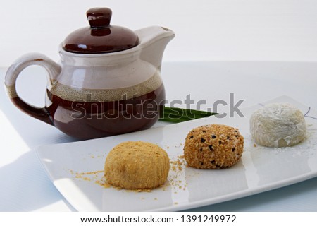 Assorted rice cake mochi set (peanut, sesame, red bean) on white plate and background, brown tea pot and bamboo leaves 