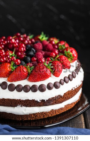 chocolate cake with strawberries, blueberries, raspberries and currants on a dark background close-up