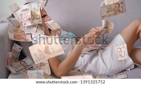 Many banknotes fly in the air overhead in slow motion. A girl lies and a lot of money falls on her. happy woman rejoices huge wealth of money.