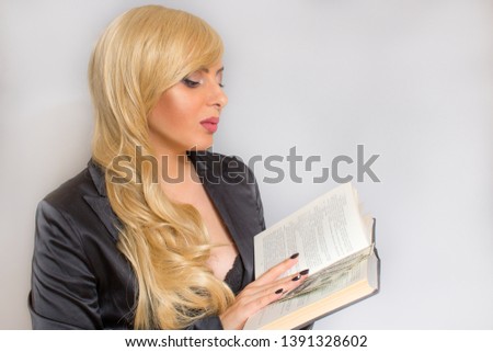 A woman with blond hair holds a book. Dollar bills are in the book. Women's book. . Woman holding a textbook. A student with a textbook in their hands. A student reads a textbook.