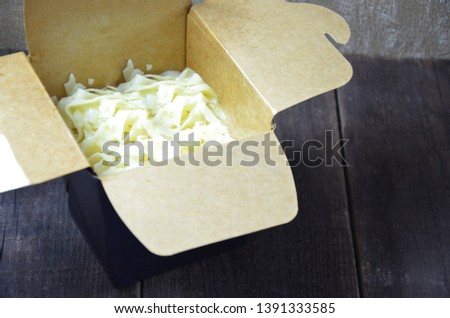 Chinese noodles in black paper box and chopsticks in hand Wok noodles. on the wooden background