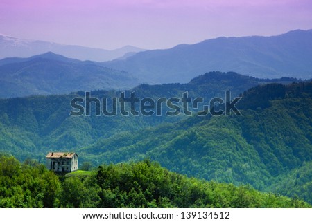 A small abandoned house in the woods and Sibillini mountains in the distance in Italy