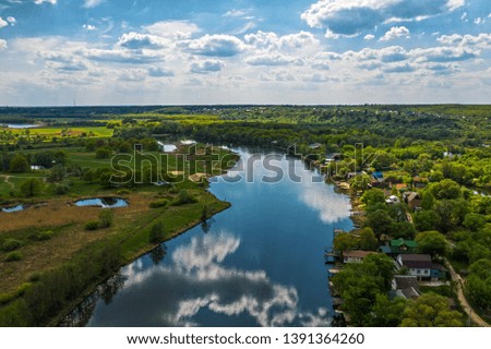 Aerial view of river with reflected blue sky and clouds, green meadows with trees and plants. Beautiful summer nature landscape from above, drone shot