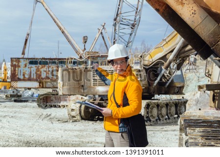 female geologist or a mining engineer amid a quarry with construction equipment discussing something, gesturing