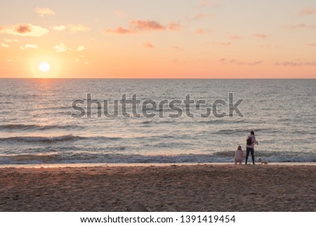 Very beautiful sunset on the Baltic Sea. In the foreground walk two girls with a dog. The sea is calm.
