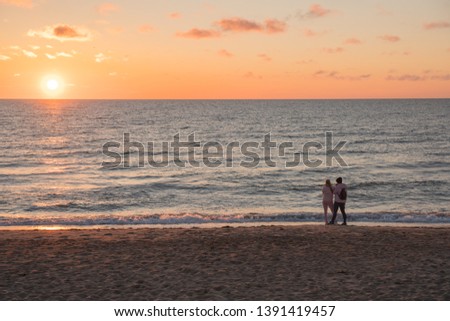Very beautiful sunset on the Baltic Sea. In the foreground walk two girls with a dog. The sea is calm.