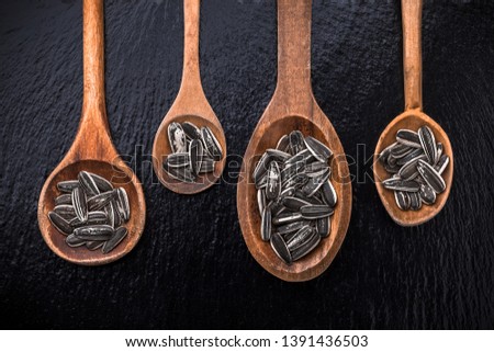 Sunflower seeds large overhead organic roasted and salted close-up arrangement in four old brown wooden spoons on black shiny stone background studio shot