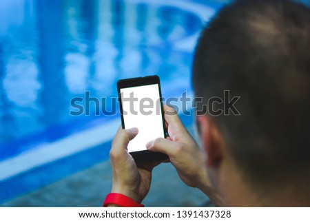 Mobility and modern lifestyle concept: young man reading a trends blog at the pool in the spa wellness center. Technology and phone addiction concept.