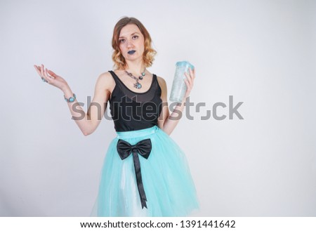 charming blonde teenager girl in a bright dress with a transparent glass of water on a white background in the Studio