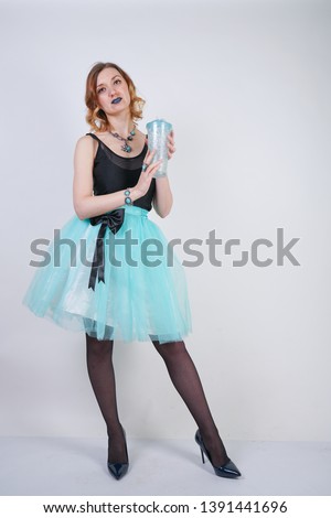 charming blonde teenager girl in a bright dress with a transparent glass of water on a white background in the Studio