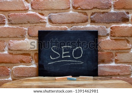 Black board with the word SEO drown by hand on wooden table on brick wall background. For business presentation.