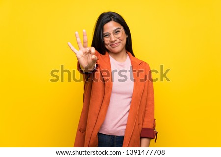 Young Colombian girl over yellow wall happy and counting three with fingers