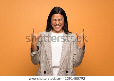 Young Colombian girl over brown wall making rock gesture