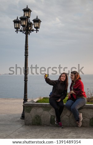 two women taking a selfie in front of the sea smiling next to a vintage streetlight
