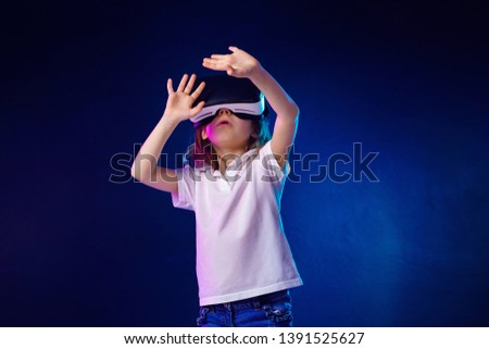 Girl 7 y.o. experiencing VR headset game on colorful background. Child using a gaming gadget for virtual reality. Futuristic goggles at young age. Virtual technology
