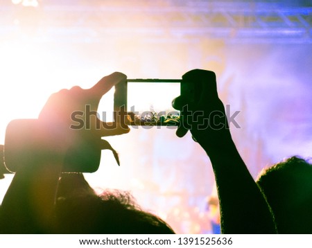Close up on a handheld smart phone, recording a live gig. Background is a defocused stage.