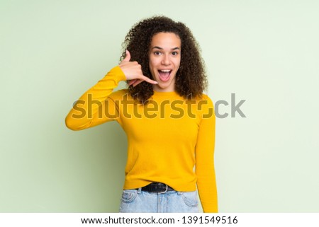 Dominican woman over isolated green background making phone gesture. Call me back sign