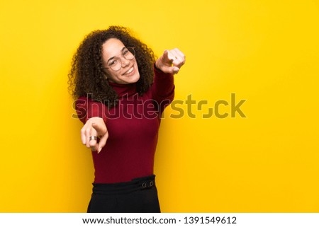 Dominican woman with turtleneck sweater points finger at you while smiling