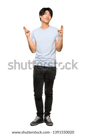 A full-length shot of a Asian man with blue shirt with fingers crossing and wishing the best over isolated white background