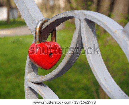 Old rusty metal red heart lock, the romantic symbol of never ending love hanging on the fence of bridge. Love forever through time concept 