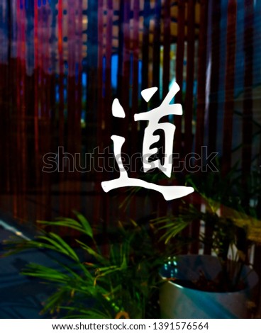 Japanese kanji calligraphy symbol 'Tao' painted on the window, bamboo and potted plants in dark background.
