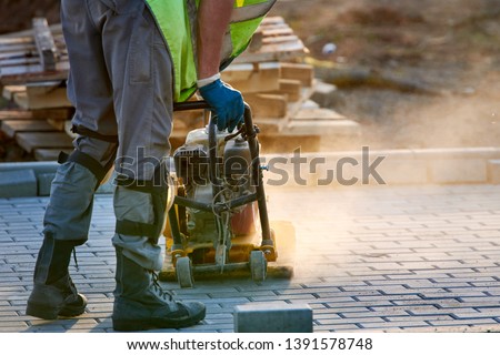 Worker in uniform and knee pads use vibratory plate compactor for path construction. Plate compactor for compaction soil or pavement or sidewalk. Indastrial equipment. Laying and tamping paving slabs Royalty-Free Stock Photo #1391578748