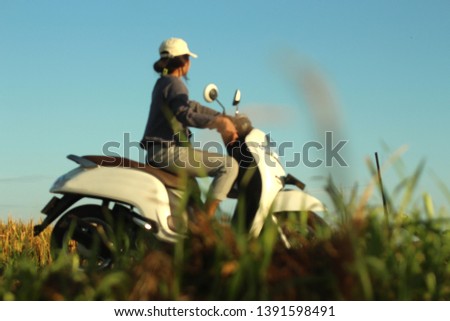 Blurry image of young woman riding motorbike in the road field. Meadow and blue sky background. Girl having fun, ride a bike. Copy space for text or design concept.