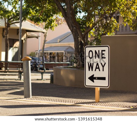 One way to the left sign in a street with tree as a background.