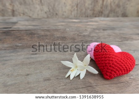Red and pink knitting hearts with Millingonia on the wooden rough table. Background of the rock wall. Sun light shines on the frame. Copy space for edting and text.