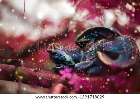 Purple and turquoise dragon laying on the branch of pink blooming tree surrounded by the sparkles. Fantastic creature in real life.