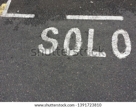 Road markings with the text SOLO reserved for solo motorcycles in white paint on standard black road surface