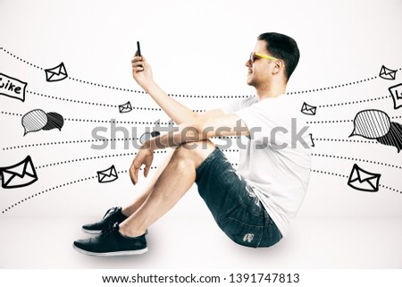 Side view of casual young guy sitting and using cellphone with communication sketch on subtle light background. Social network and media concept 