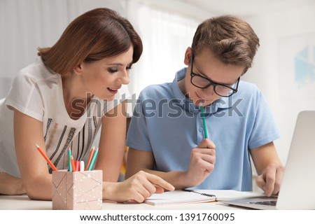 Mother helping her teenager son with homework indoors Royalty-Free Stock Photo #1391760095
