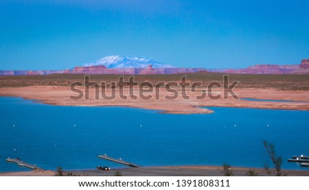 Lake Powell in northern Arizona offers beautiful vistas of red rock formations at sunset, blue waters, beaches, marina, desert sky and in the distance snow capped mountains in this vacation destinatio
