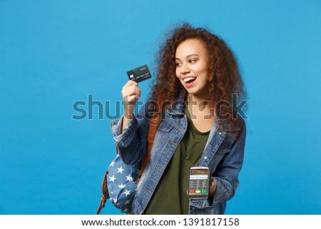 Young african american girl teen student in denim clothes backpack hold credit card isolated on blue background studio portrait. Education in high school university college concept Mock up copy space
