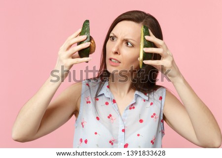 Concerned young woman in summer clothes holding two halfs of fresh ripe avocado fruit isolated on pink pastel background in studio. People vivid lifestyle relax vacation concept. Mock up copy space