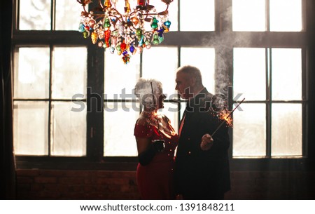 old couple in love - a woman in a red dress and a gray-haired man in a black suit on the anniversary of their wedding burn fireworks and lights and passionately embrace