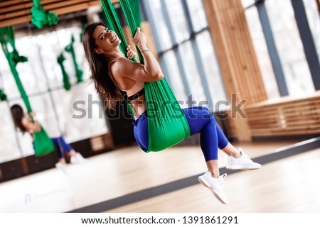 Beautiful young brunette girl is on the aerial silks next to the big mirror in the modern gym