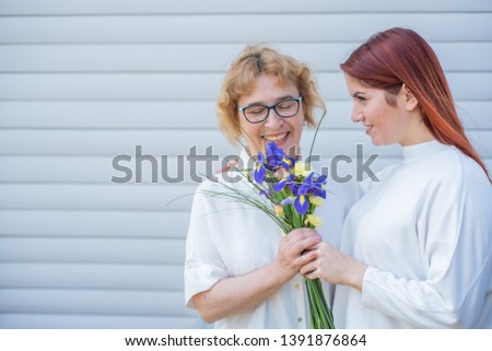 Adult daughter gives flowers to her mother outside, in the courtyard of the house. Spending time together, celebrating at home on weekends. Mothers Day. Warm intergenerational relationships
